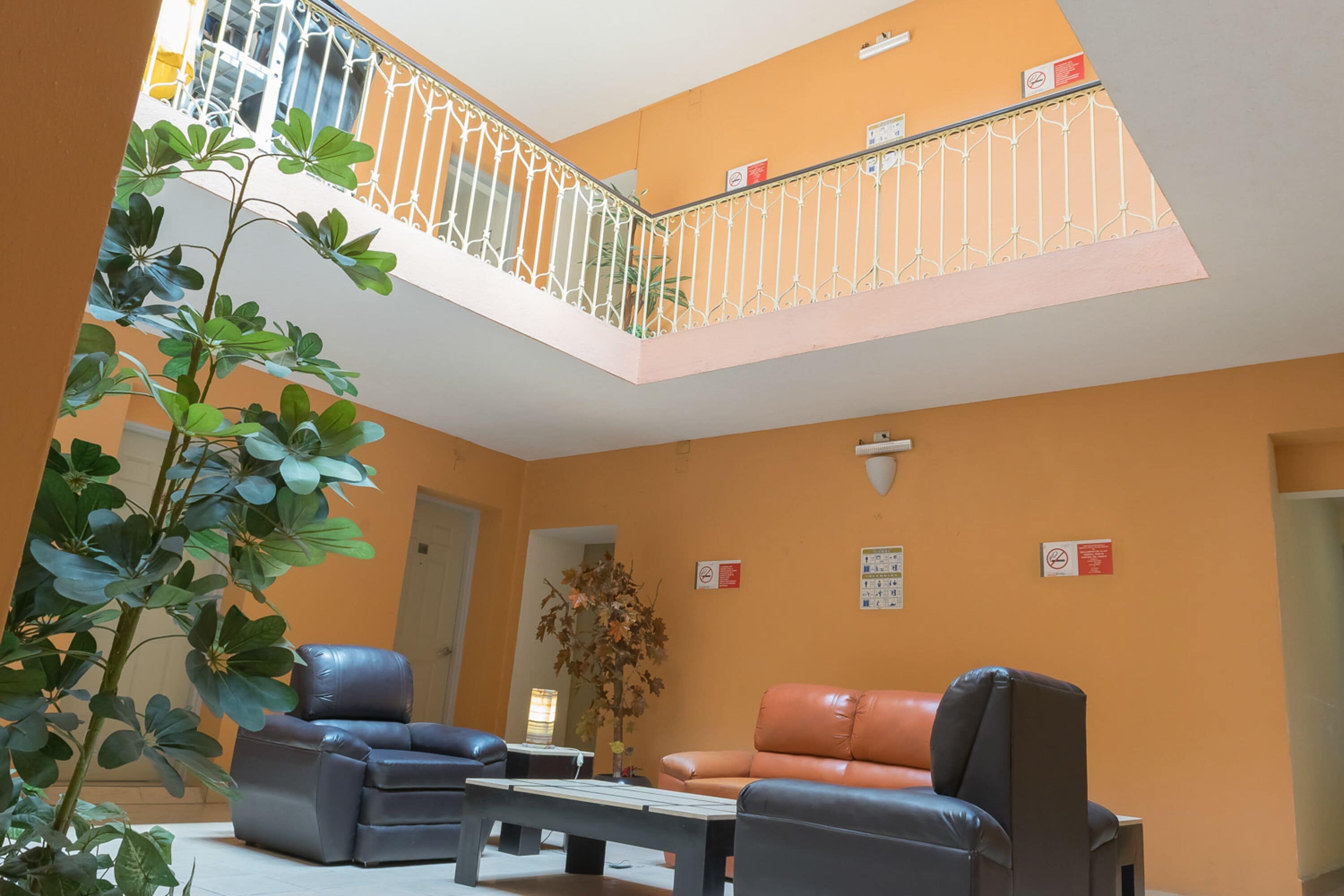 A spacious indoor area with a high ceiling, a balcony with a metal railing, and seating arrangements including a sofa and chairs.