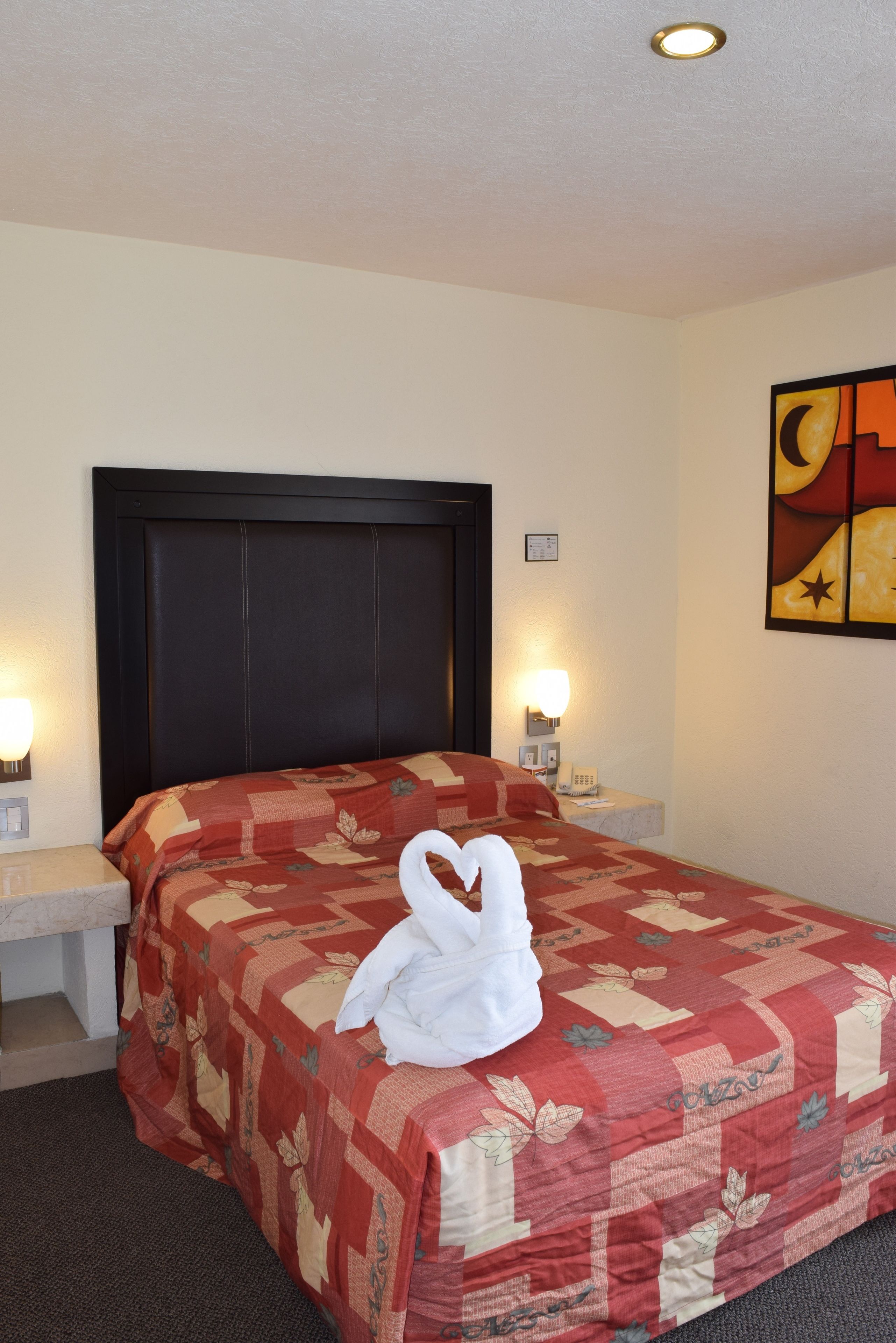 Una habitación de hotel con una cama grande, dos mesitas de noche con lámparas, una obra de arte en la pared y una lámpara de techo.