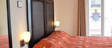 Una habitación de hotel con una cama grande, una mesita de noche con teléfono, un espejo y una ventana con cortinas.