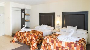 Habitación de hotel con dos camas, cada una con una colcha estampada y una toalla con forma de cisne. Entre las camas, un mesita de noche con un teléfono y una lámpara.