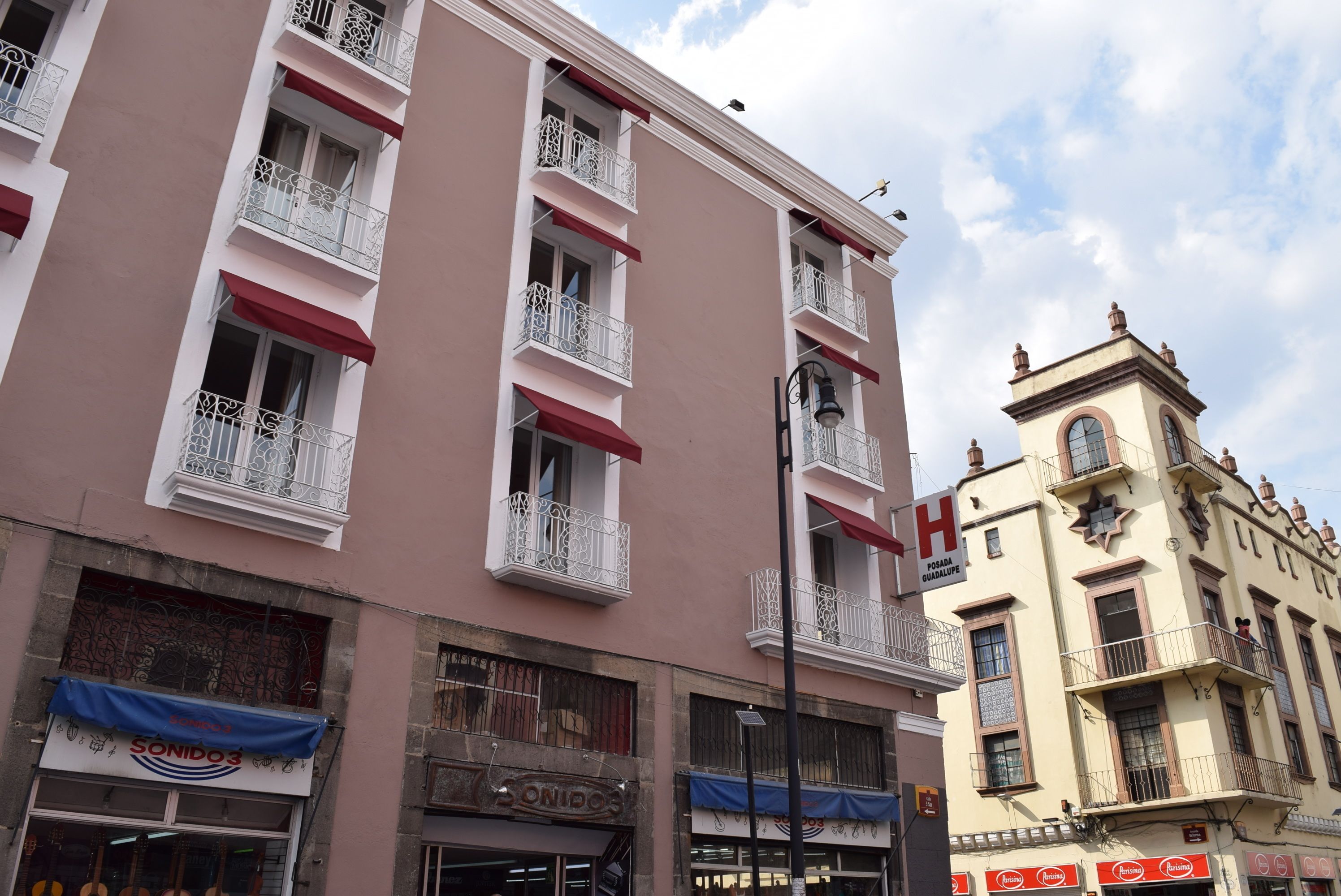 A multi-story building with balconies, a visible 'H' sign indicating a hotel, and storefronts with awnings.
