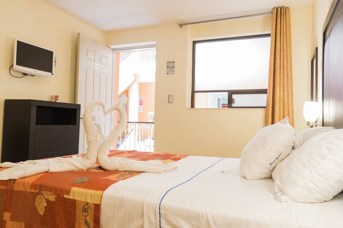 A hotel room with a bed, a TV, a desk, and a window with curtains.