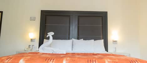 Une chambre d’hôtel avec un grand lit, deux lampes de chevet, un téléphone et un cygne décoratif posé sur les oreillers.