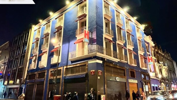 Un hotel con varios balcones, un letrero grande con la letra 'H' y un comercio con persianas cerradas.