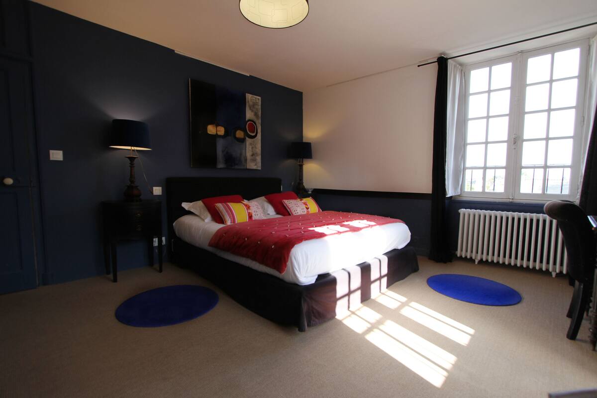A bedroom with a large bed, two bedside tables, a radiator, and a window with curtains.