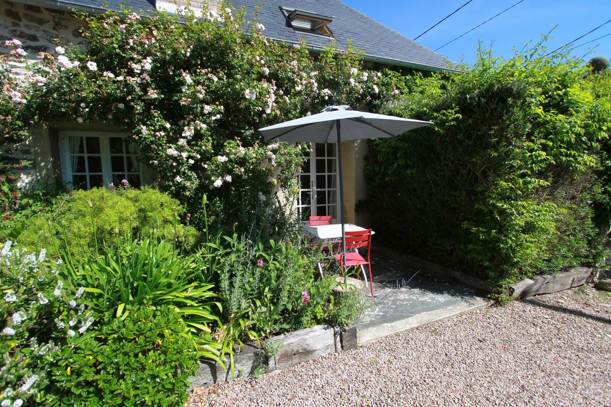 A garden with a table and chairs, surrounded by lush greenery and flowering plants.
