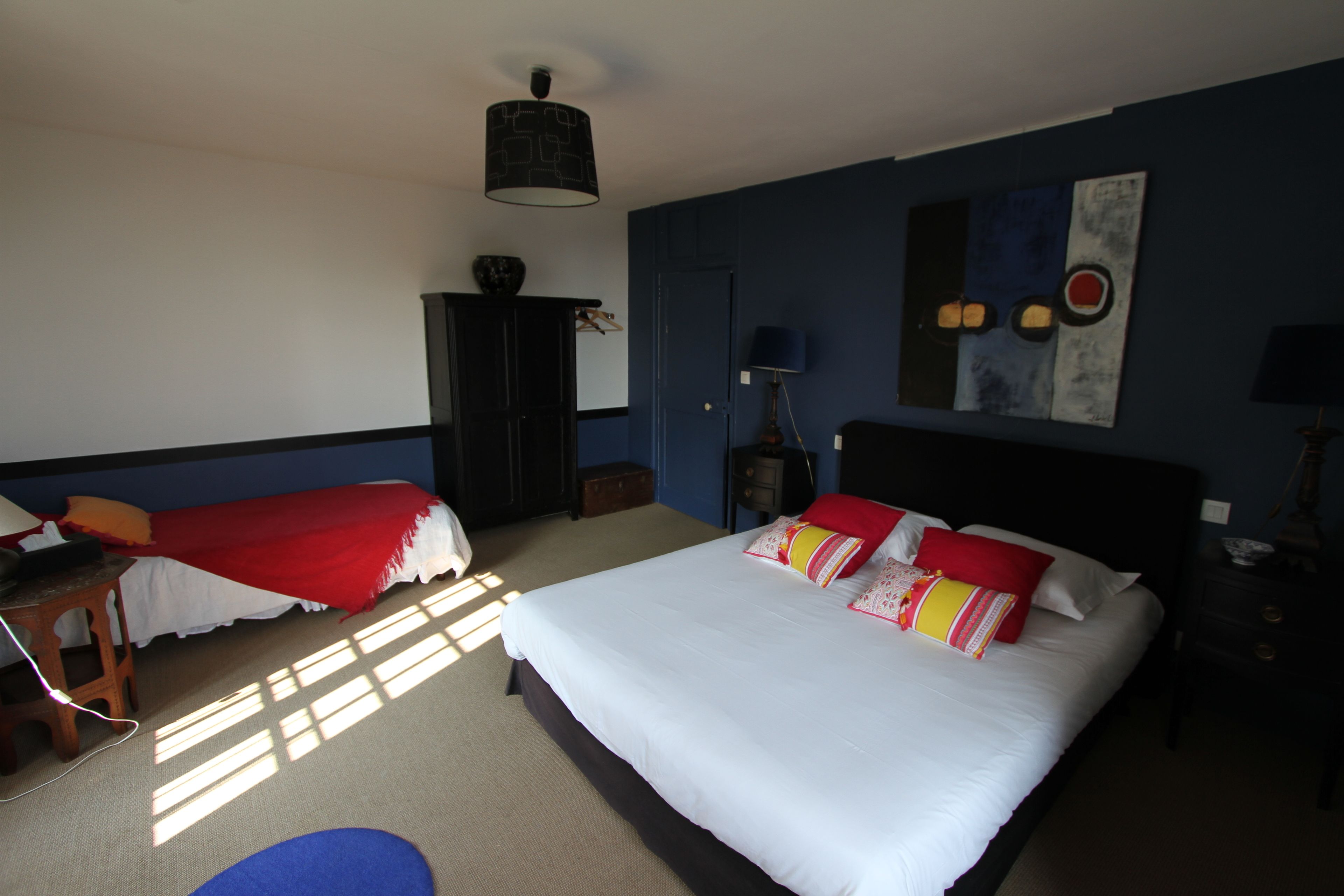 A hotel room with a large bed, a smaller bed, a wardrobe, a desk, and a lamp.