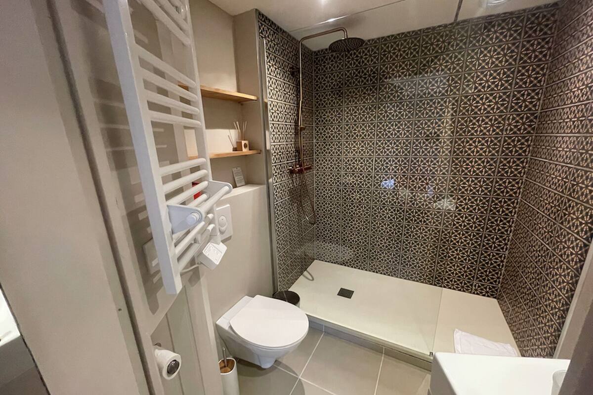 A bathroom with a toilet, a shower with patterned tiles, and a towel rack.