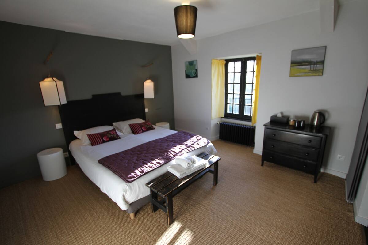 A bedroom with a bed, bedside tables, a bench, a radiator, and a window with curtains.
