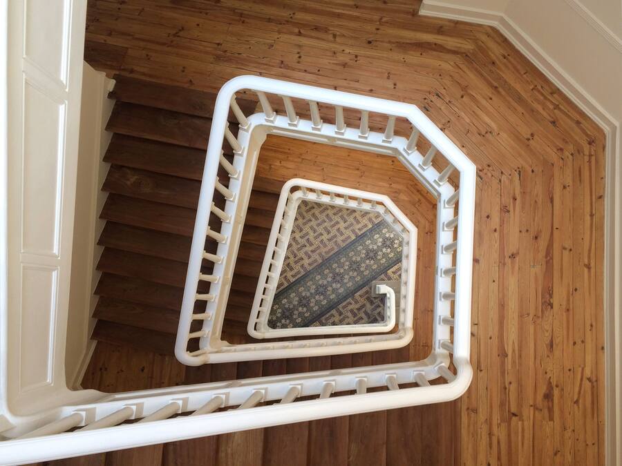 A wooden staircase with a white handrail and a patterned carpet.