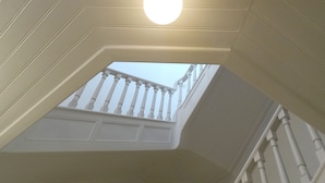 Une vue depuis une fenêtre donnant sur un balcon avec des balustrades blanches et un luminaire rond au plafond.
