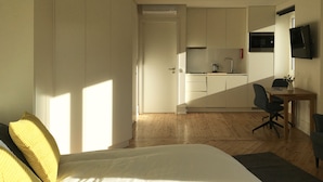 Une chambre à coucher avec un lit, un bureau et un coin cuisine à l’arrière-plan.