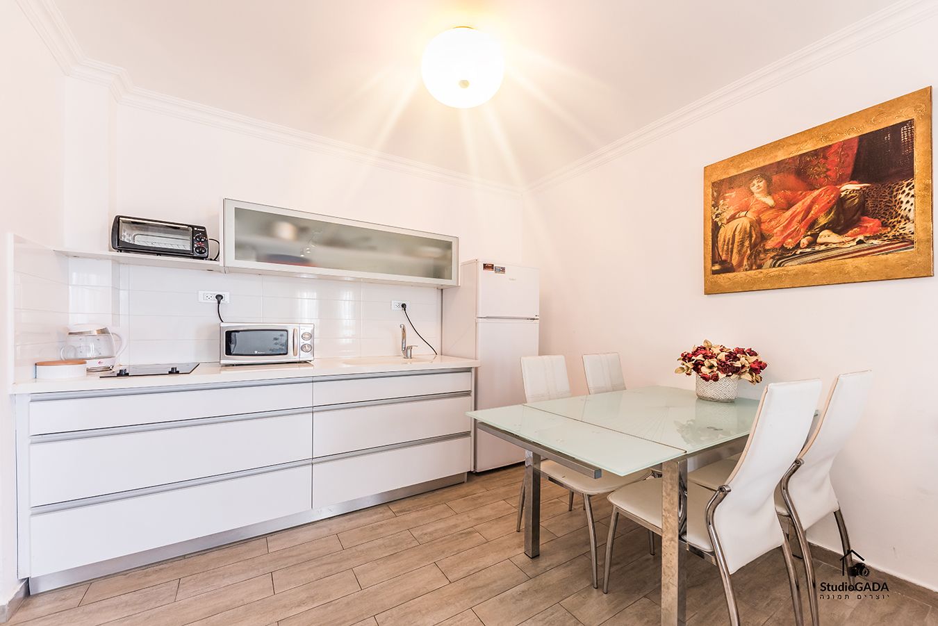 A modern kitchen with white cabinetry, a microwave, a toaster, and a glass dining table with chairs.