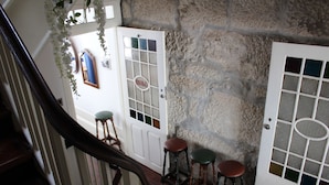 A staircase with a wooden handrail, a white door with a glass panel, and two stools with cushions. - Linha22 GuestHouse (Porto)