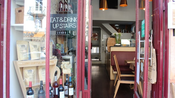 A restaurant with a sign reading "EAT & DRINK UPSTAIRS" and a display of Luso coffee roasters. - Linha22 GuestHouse (Porto)