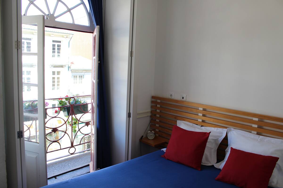 A bedroom with a bed, a wooden headboard, and a window with a view of buildings.