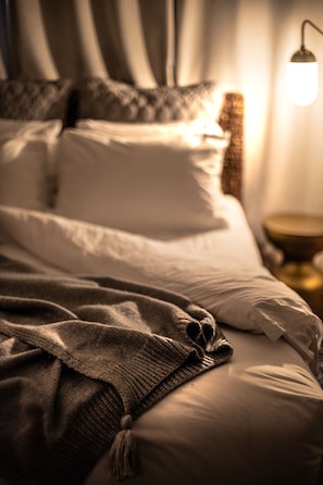 A bed with white linens and a brown blanket, a bedside lamp, and a nightstand with a gold-colored object. - The Sailmaker's House (Portsmouth)