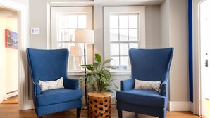 Two blue armchairs with matching cushions, a wooden side table with a woven pattern, and a potted plant between them. - The Sailmaker's House (Portsmouth)