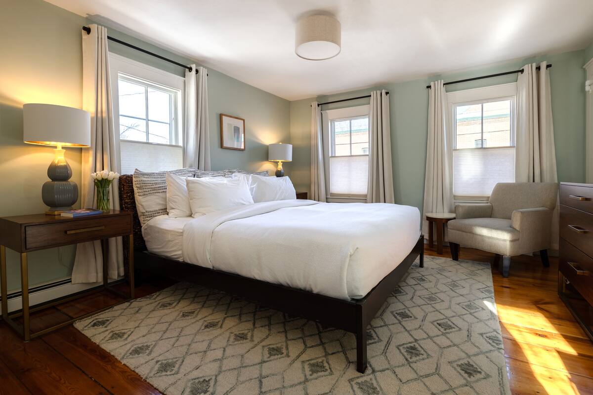 A neatly arranged bedroom with a large bed, bedside lamps, a chair, and a dresser.