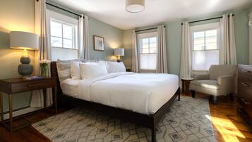 Une chambre à coucher bien rangée, avec un grand lit, des lampes de chevet, une chaise et une commode.