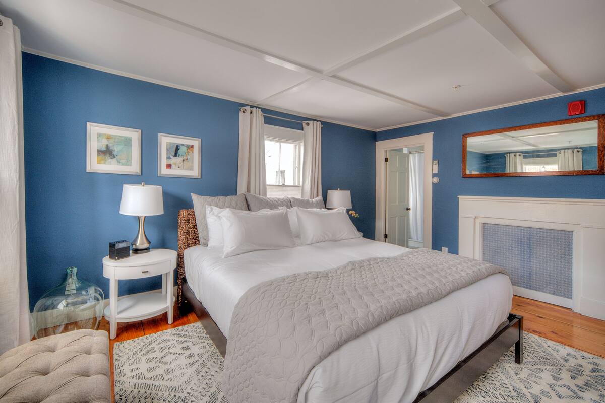 A bedroom with a large bed, two bedside tables, a nightstand, a mirror, and a fireplace.
