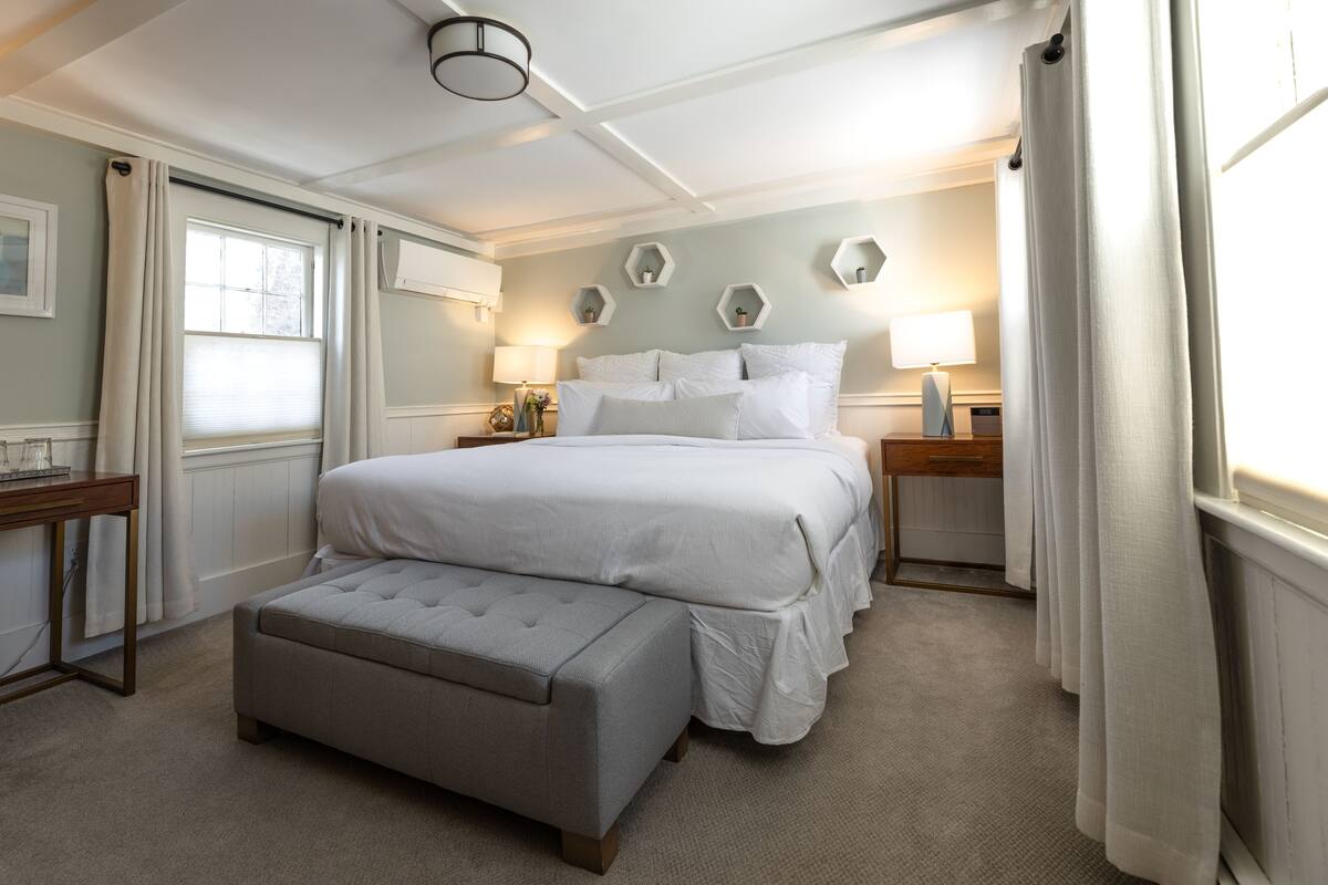 A bedroom with a large bed, a nightstand, a lamp, and a window with curtains.