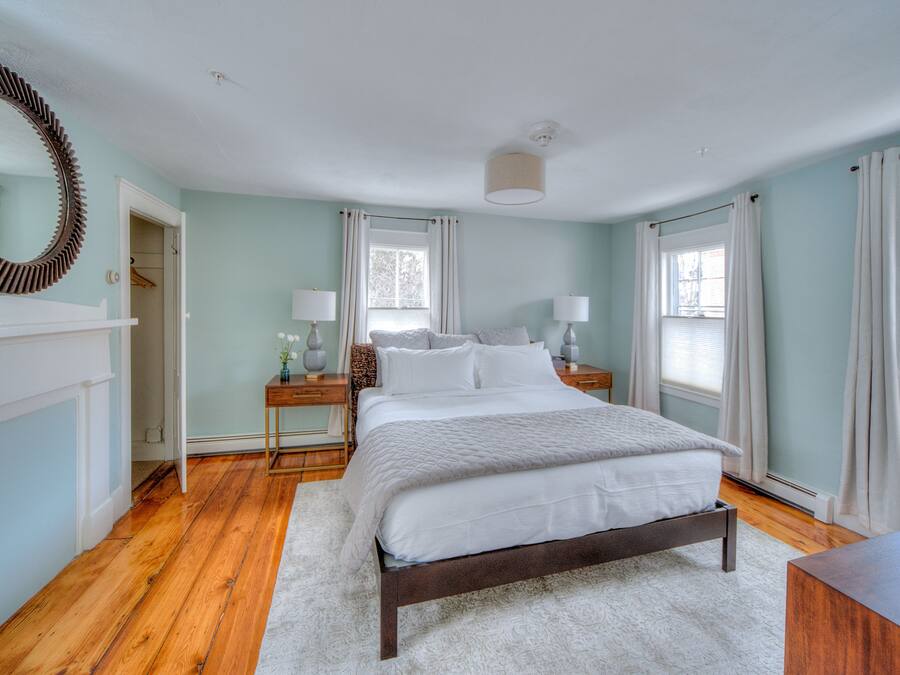 A bedroom with a bed, bedside tables, a mirror, and a window with curtains.