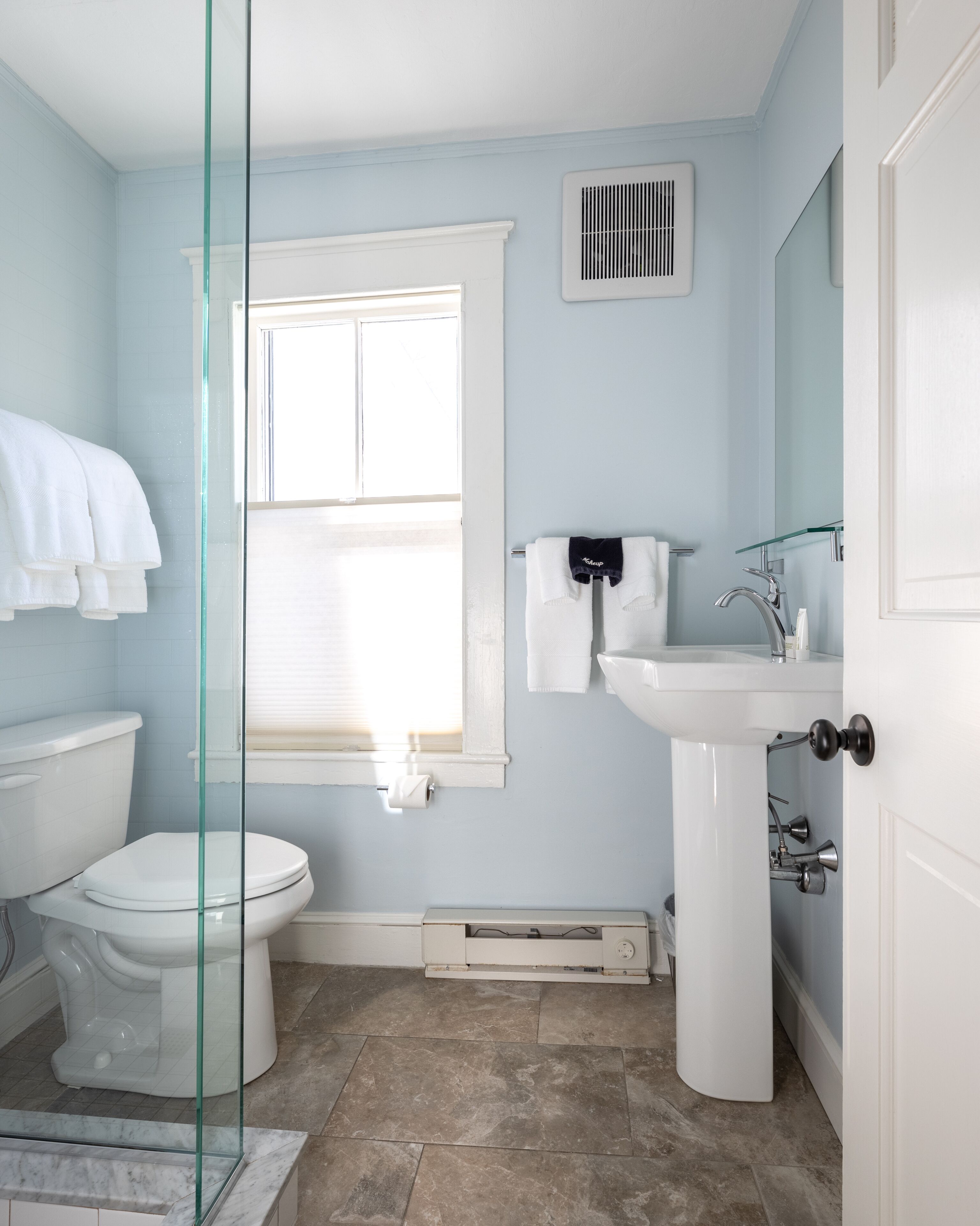 Ein Badezimmer mit Toilette, Waschbecken, Fenster und einer Duschkabine aus Glas.