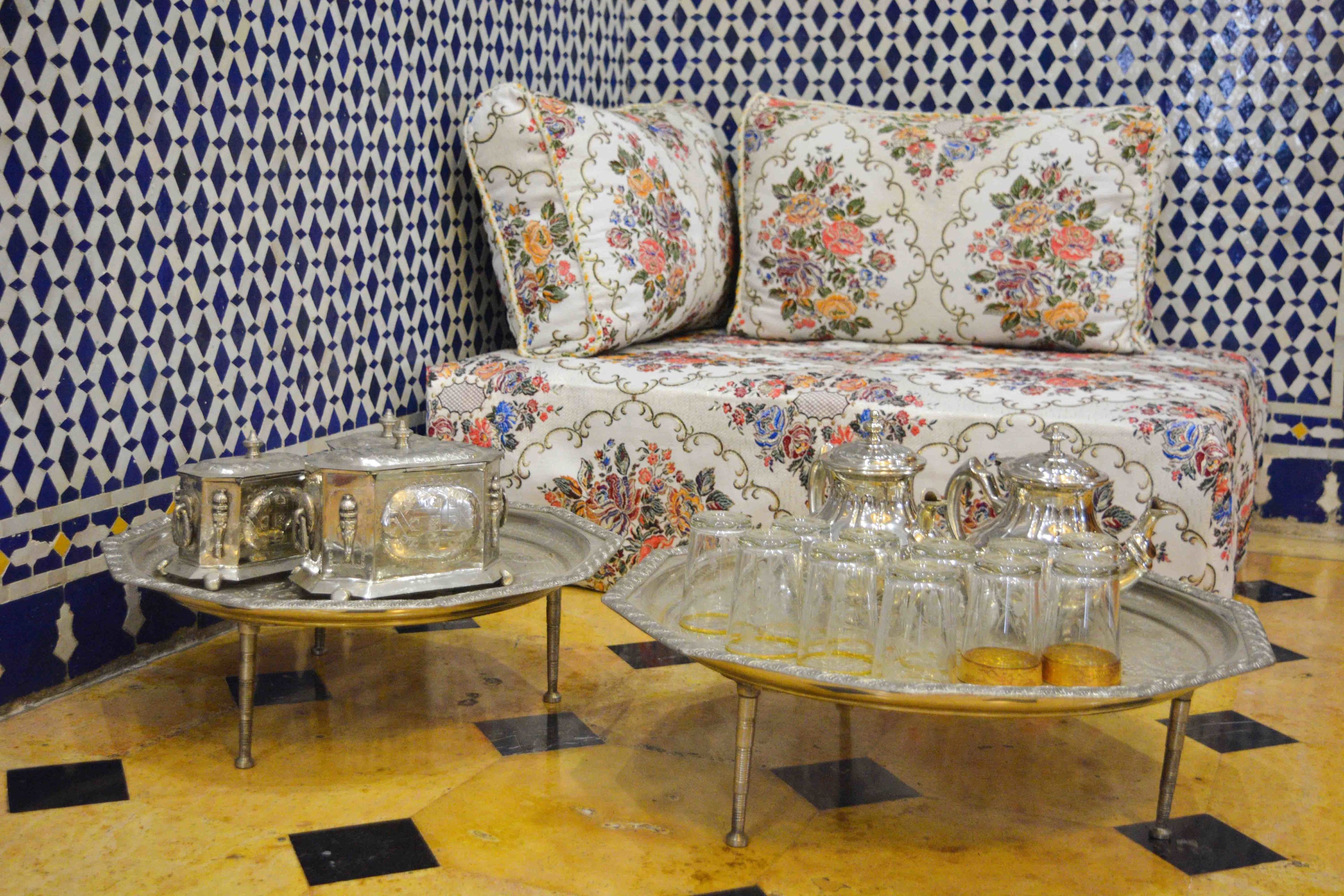 A room with a patterned blue and white wall, a sofa with floral upholstery, and a tray table with silverware and glassware.