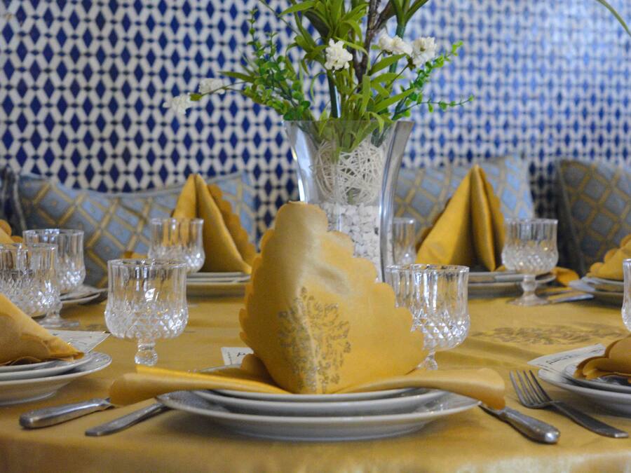 A dining table set with yellow napkins, clear glassware, and a vase with white flowers.