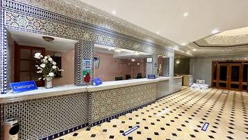 A hotel reception area with a patterned wall, a reception desk, and a tiled floor.
