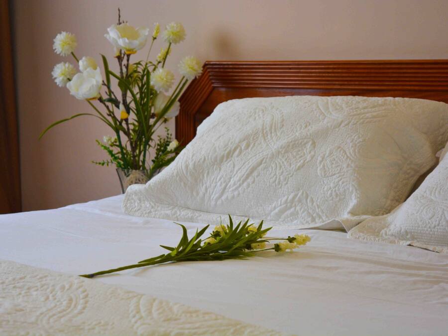 Ein ordentlich bezogenes Bett mit weißen Leinen und Kissen, ein hölzernes Kopfteil und ein Blumenvasen auf dem Beistelltisch.