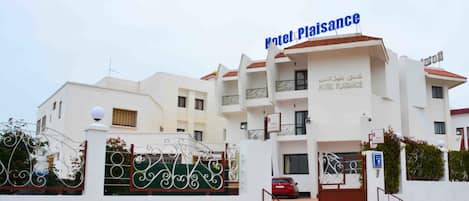 A multi-story hotel building with a sign reading "Hotel Plaisance" in both English and Arabic.