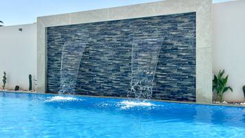 Piscina con una cascada moderna y un muro de piedra.