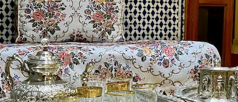 A room with a patterned sofa, a tray table with glassware, and a decorative teapot.