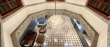 Una stanza ottagonale con pavimento decorato, un lampadario e un angolo salotto con divano e poltrone.