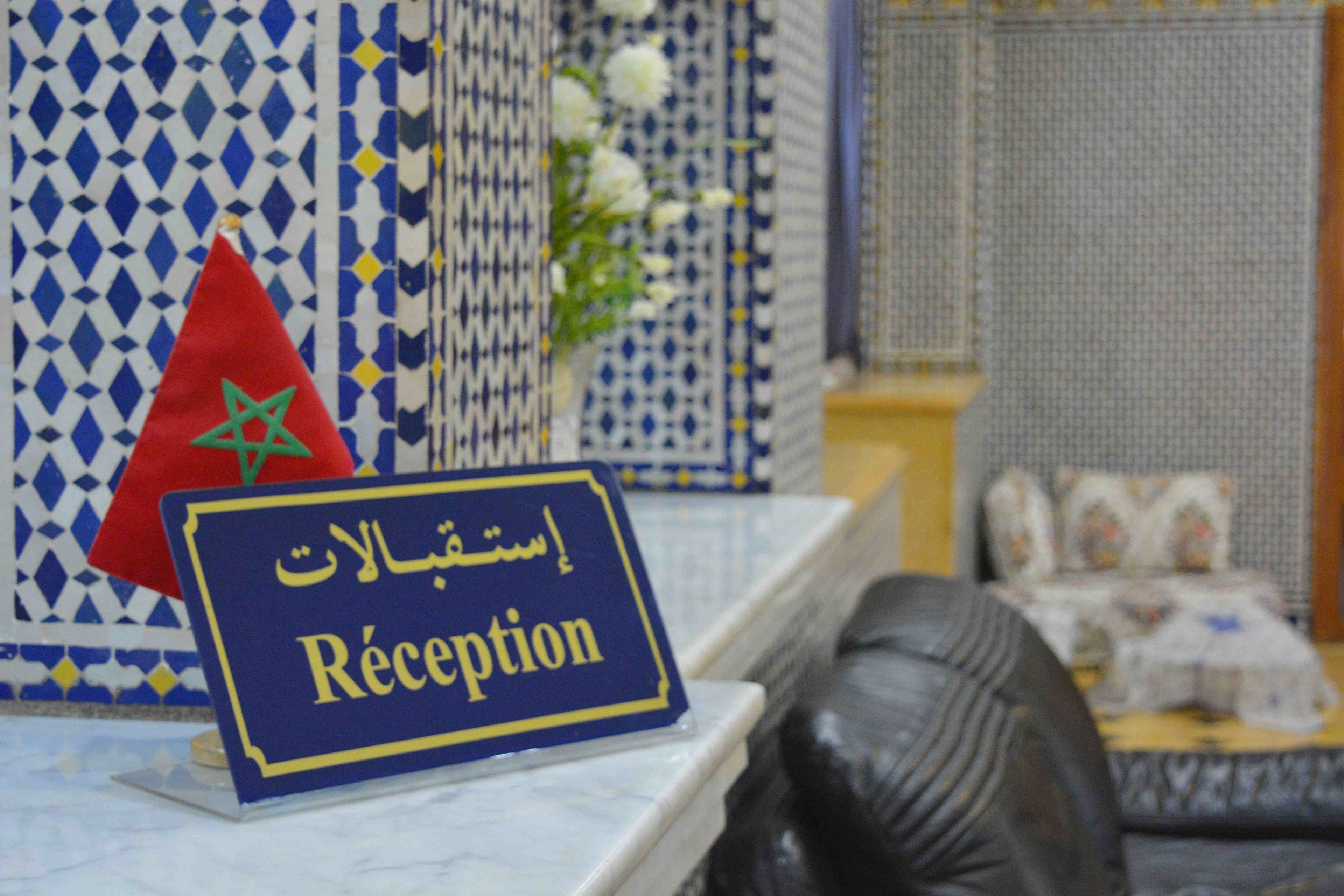 A reception area with a sign in Arabic and English, a Moroccan flag, and a patterned wall.