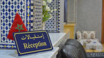 A reception area with a sign in Arabic and English, a Moroccan flag, and a patterned wall.