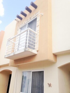 Un edificio con balcón, una ventana con cortinas y una pequeña decoración con forma de mariposa.