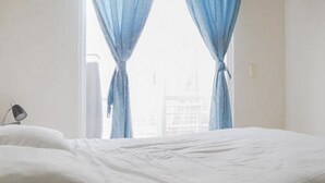 Habitación de hotel con cama, lámpara y ventana con cortinas azules.