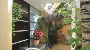 A narrow pathway leading to a house with a black garage door, surrounded by various potted plants and a small table. - Casa Vacacional Cancún 3270 by Sinbad (Cancun)