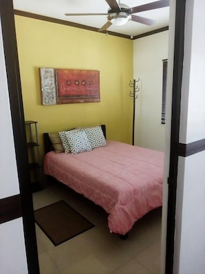 A bedroom with a bed, a ceiling fan, a wall-mounted artwork, and a radiator.