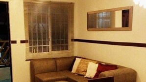 A living room with a sofa, ottoman, dining table, chairs, a ceiling fan, and a window with blinds. - Apartamento Real Ibiza 639 by Sinbad (Playa del Carmen)