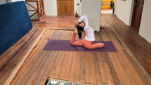 A person performing a yoga pose on a mat in a hallway with wooden flooring, a wooden door, and a fire extinguisher sign. - Casa Intihuatana - Hostel (Pisac)