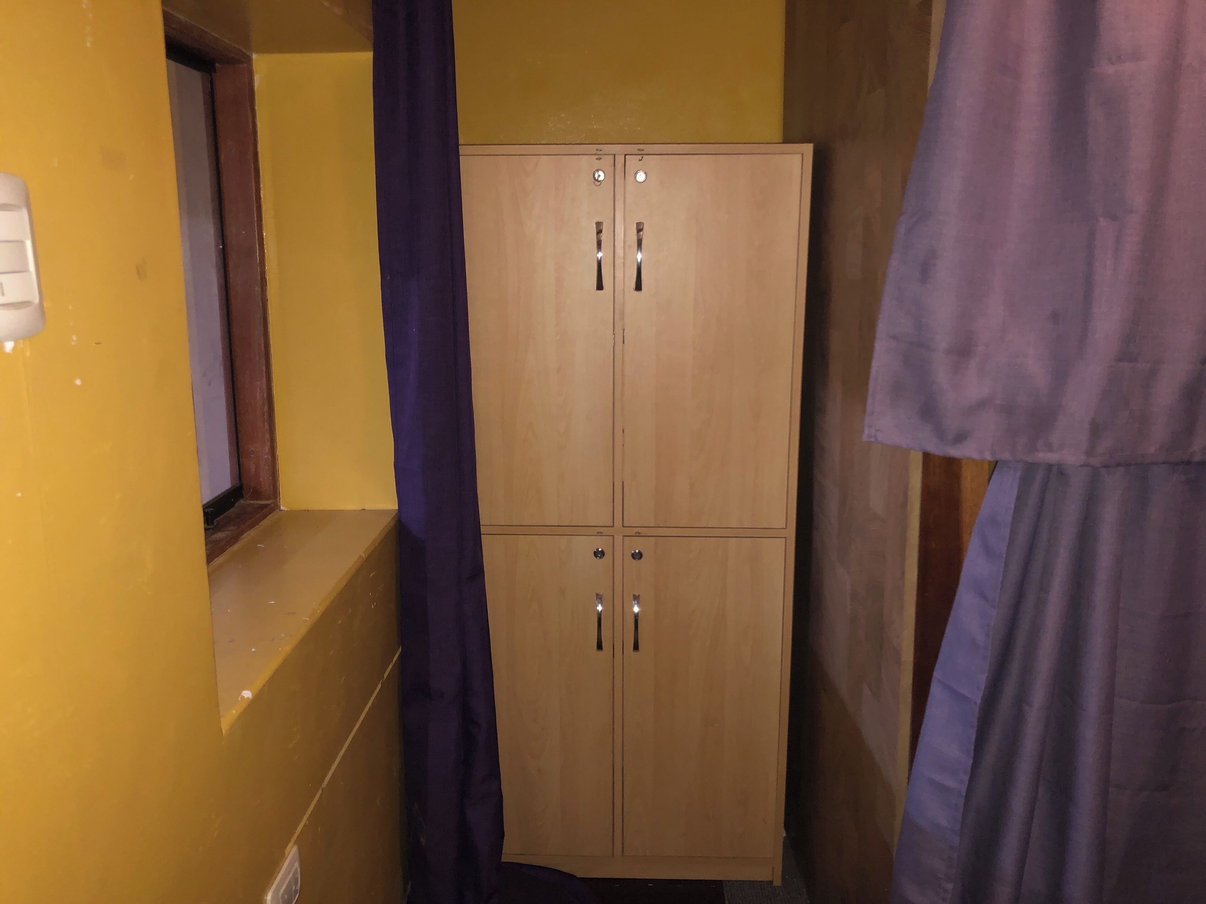 Un armari de fusta amb dues portes i una nansa, situat en un passadís estret amb parets grogues.