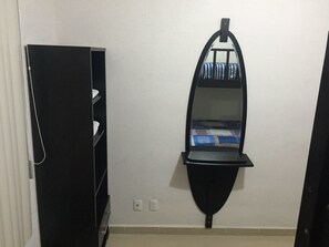 A room with a black wardrobe, a mirror with a shelf, and a bed with a striped blanket.