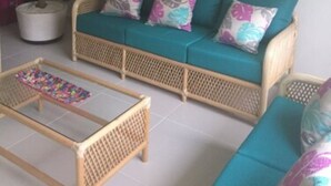 A wicker sofa with teal cushions and floral pillows, a woven coffee table, and a potted plant. - Residencial Allegranza 628 by Sinbad (Playa del Carmen)