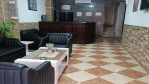 A lobby with a checkered floor, leather seating, a reception desk, and a wall-mounted air conditioner. - Al-Nujoom Hotel Suites (Amman)