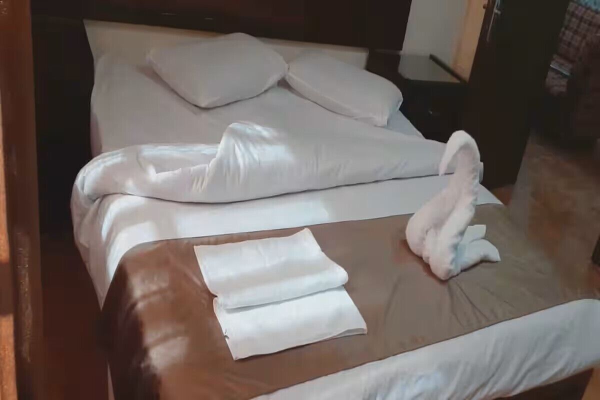 A neatly made bed with white linens and a brown headboard.