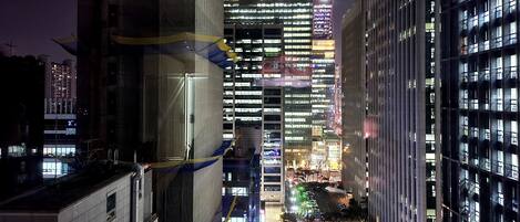 A nighttime cityscape with modern buildings, including a prominent 'posco' sign on a high-rise.